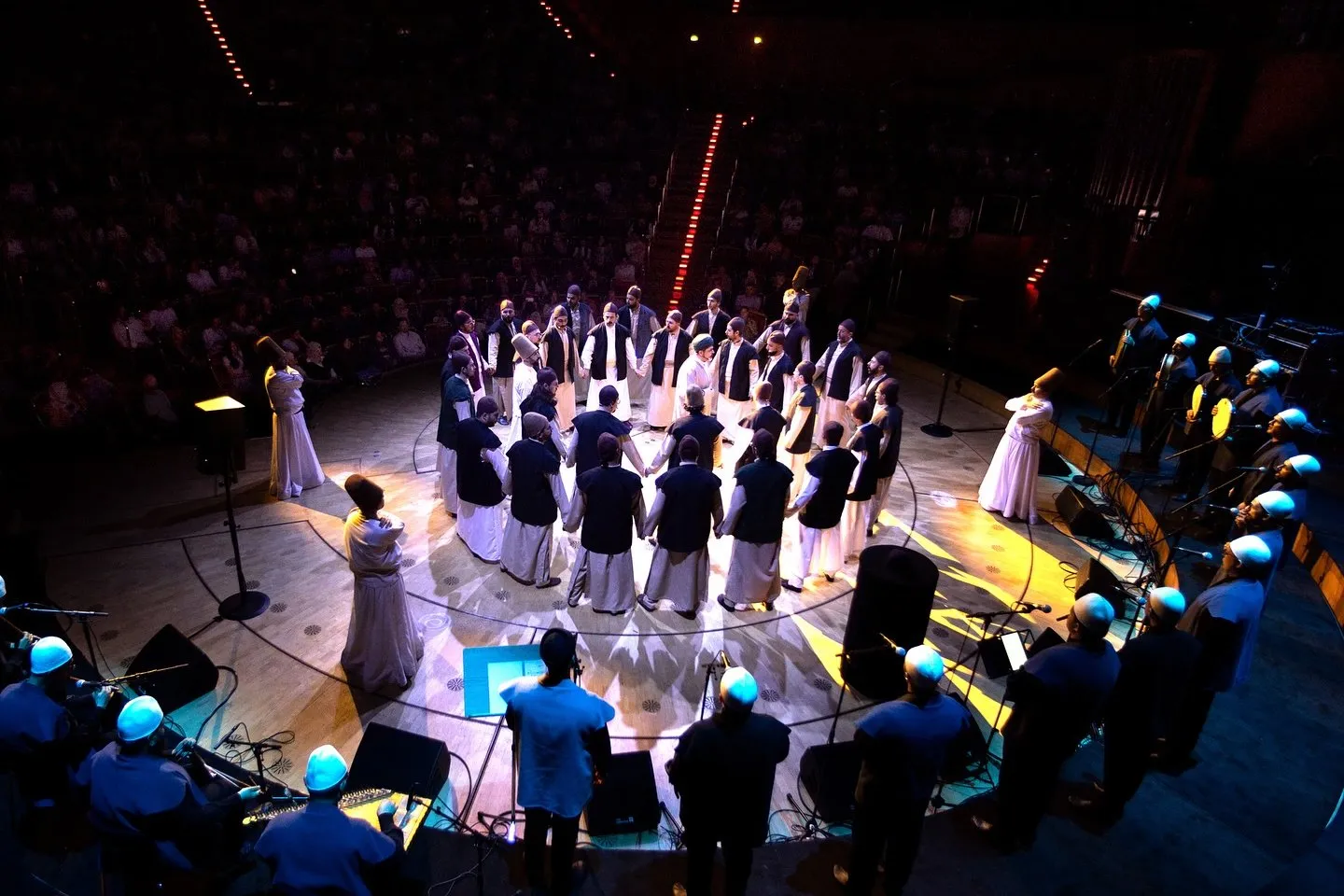 Sufi Devran in der Kölner Philharmonie am 30.05.2025: das Ensemble im Kreis auf der Bühne, davor der besetzte Saal