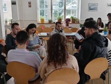 Teilnehmende von Zero Plate sitzen in Kleingruppen an Tischen und arbeiten zusammen